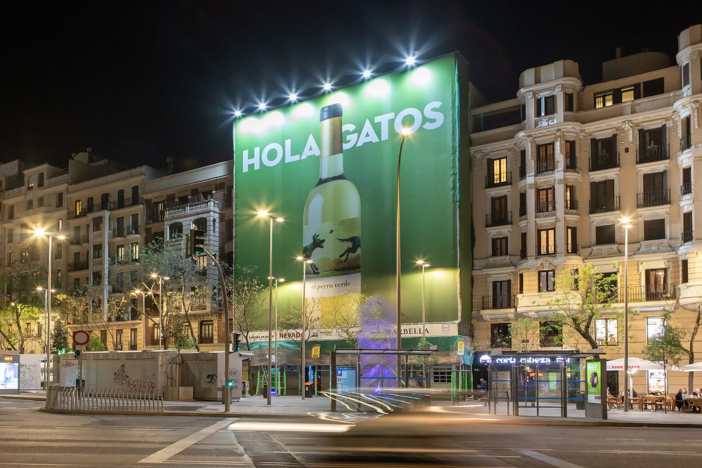 Fachada de un edificio de Barcelona cubierta de noche por una lona publicitaria con el rótulo Hola Gatos