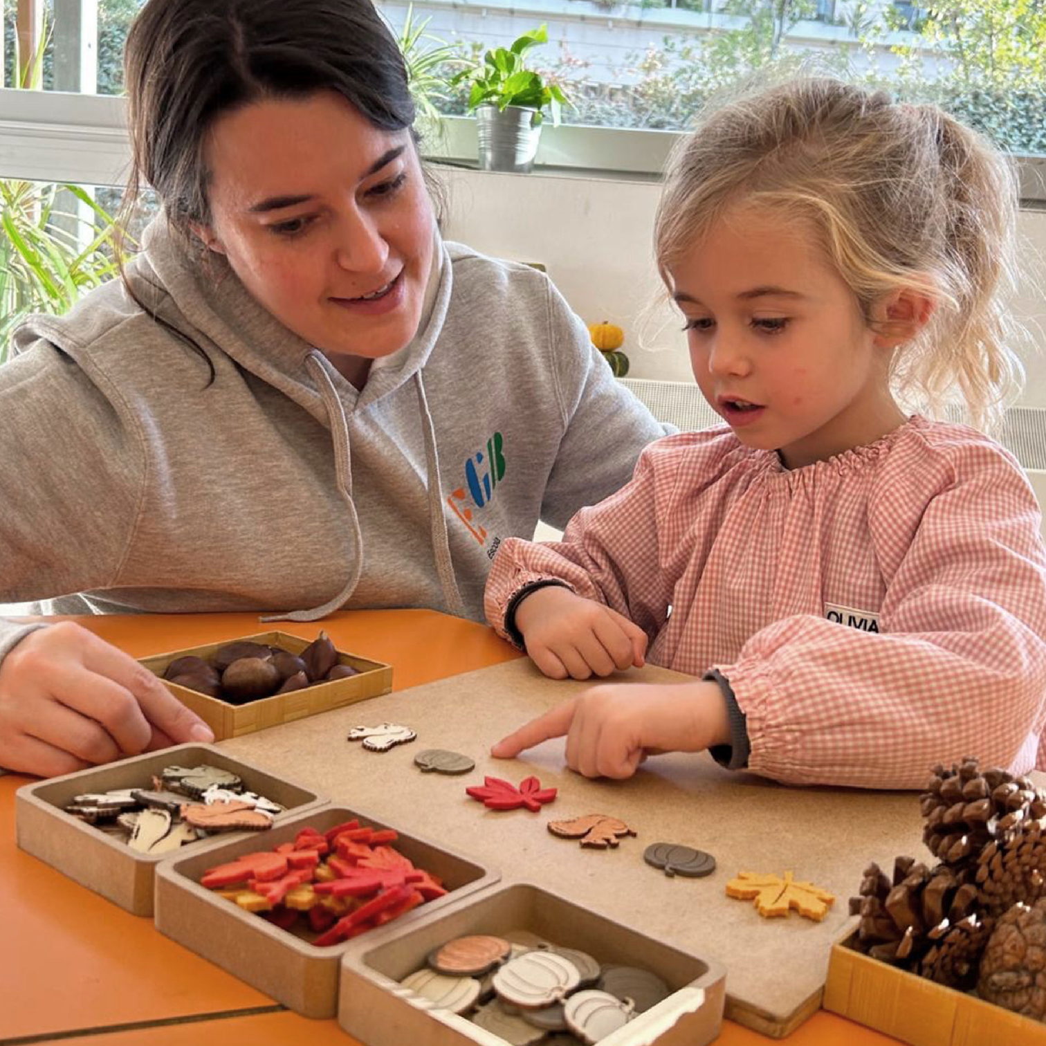 Una educadora y una niña clasifican piezas de madera y botones en una bandeja de juego