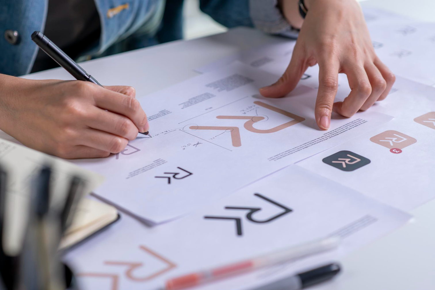 Dos manos revisan bocetos de logotipo impresos sobre una lámina de papel