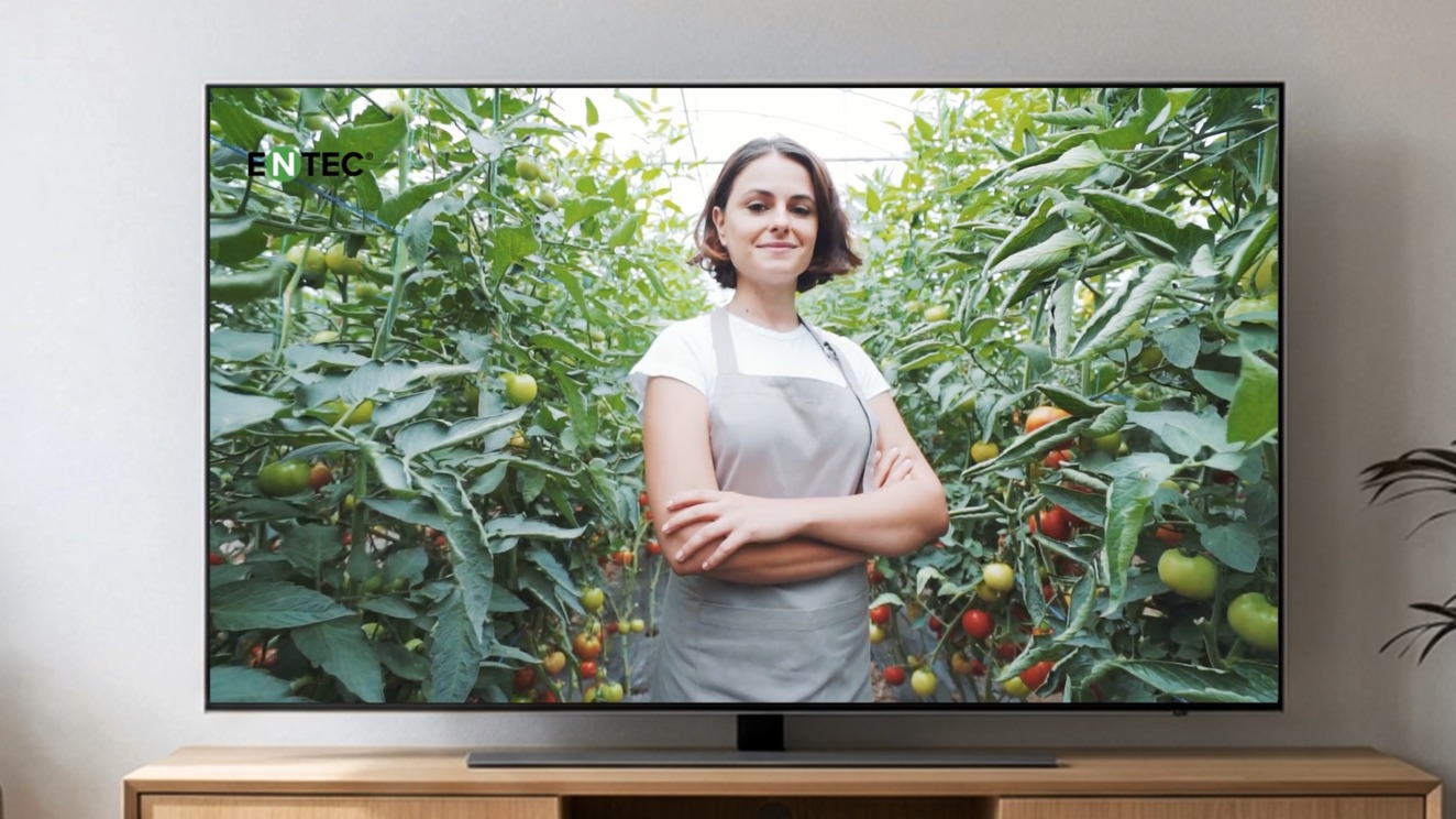 Televisor emitiendo el anuncio de ENTEC: una agricultora de brazos cruzados entre tomateras de invernadero