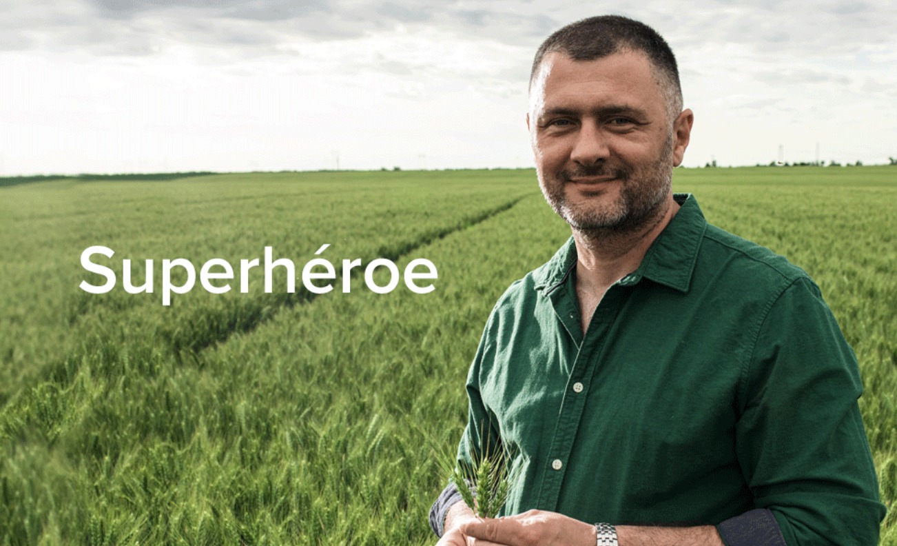 Agricultor sonriente en un campo de cereal verde, con el rótulo «Superhéroe» de la campaña de EuroChem