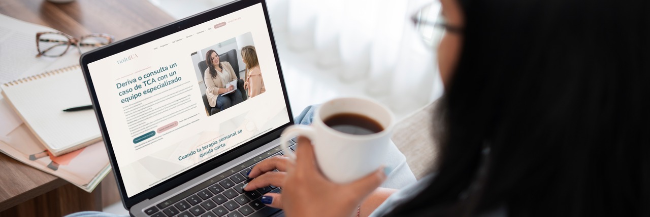 Una mujer con una taza de café navega por la web de NaluTCA en un portátil